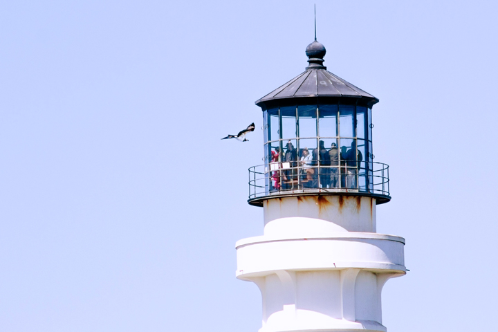people in small glass turret atop lighthouse